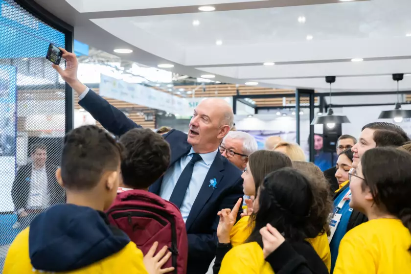 Photographie événementielle du Ministre de l'industrie Roland Lescure réalisant un selfie devant des collégiens dans un salon profesionnel